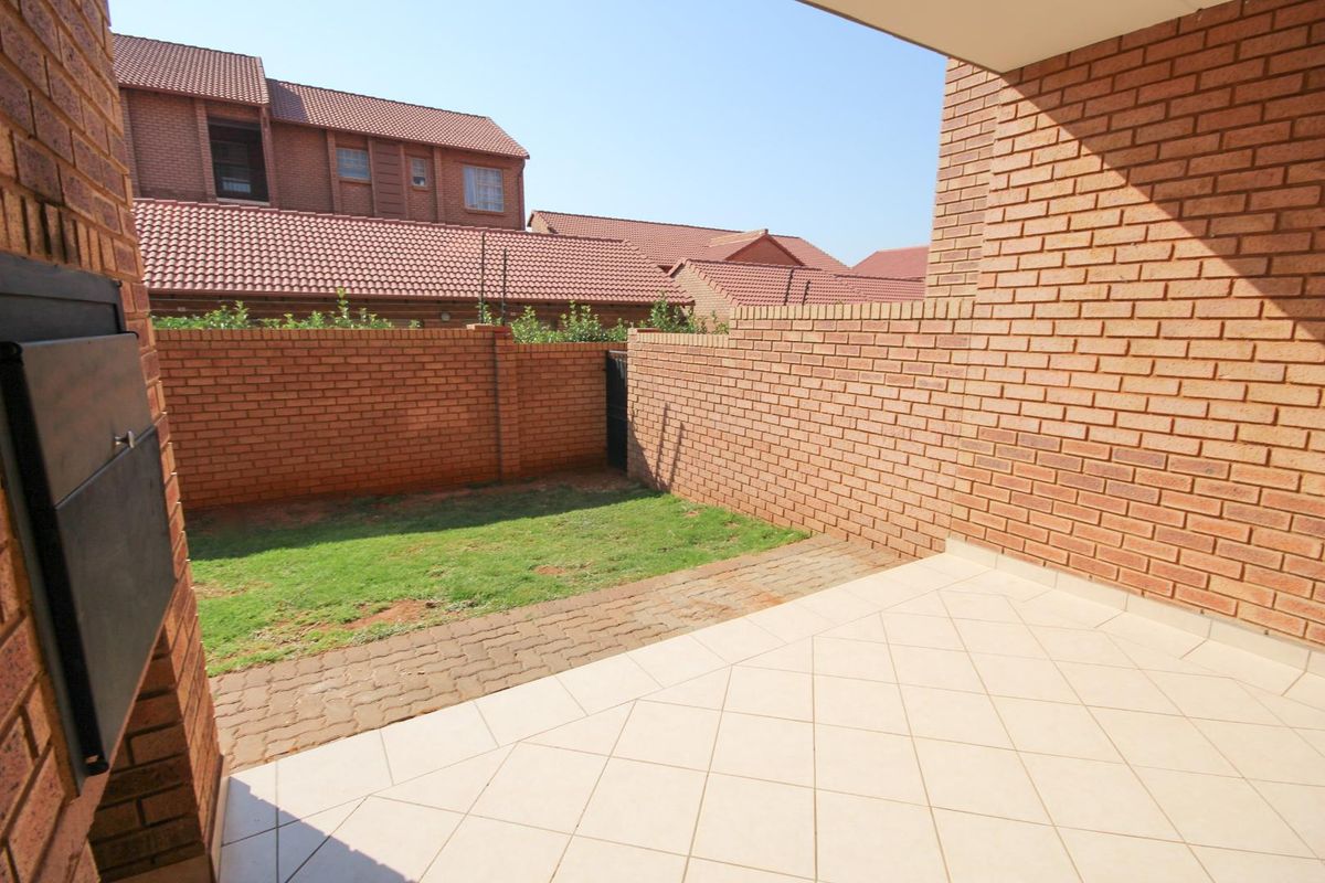 A private rear courtyard featuring a tiled patio area, paved walkway, and a small lawn enclosed by brick boundary walls.