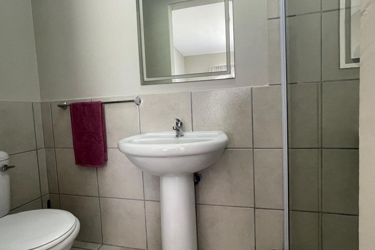 A functional bathroom featuring a pedestal sink, wall-mounted mirror, toilet, and a tiled shower enclosure.