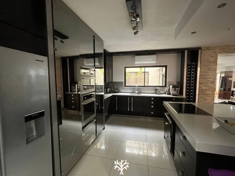 Modern kitchen featuring dark cabinetry, stone countertops, a central island, built-in appliances, and tiled flooring with recessed lighting.