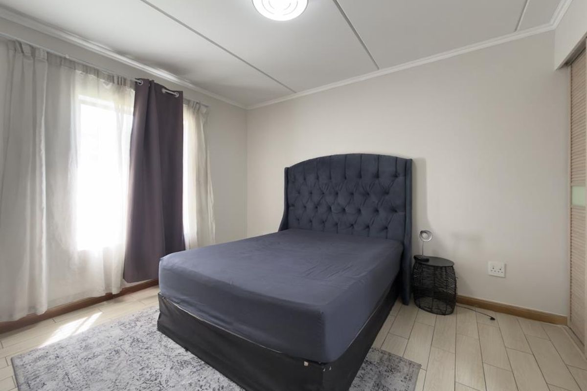 A well-lit bedroom featuring tiled flooring, a built-in wardrobe with sliding doors, and a central ceiling light fixture.