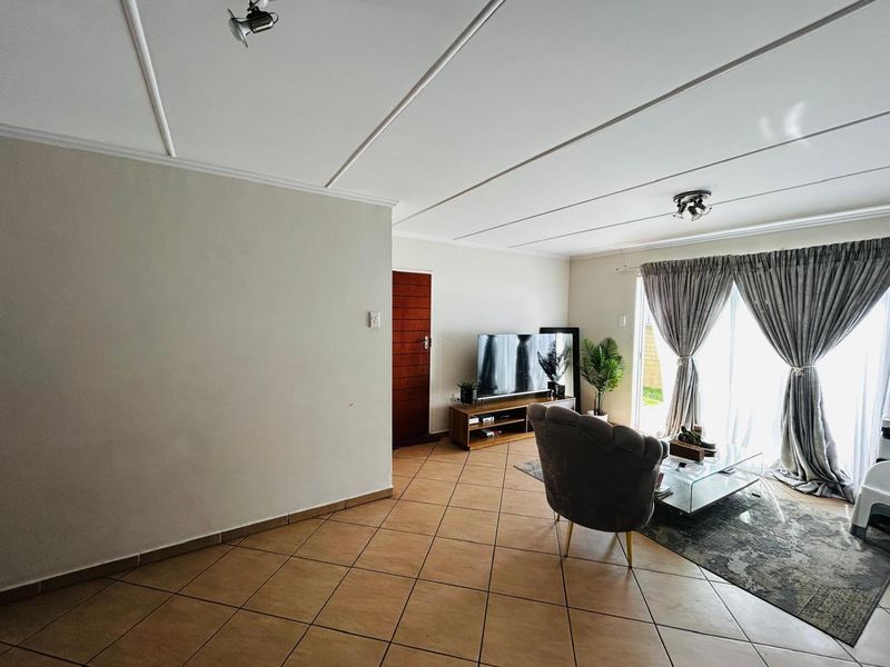 A living room featuring tiled flooring, a panelled ceiling with spotlights, and a sliding glass door providing access to the exterior.