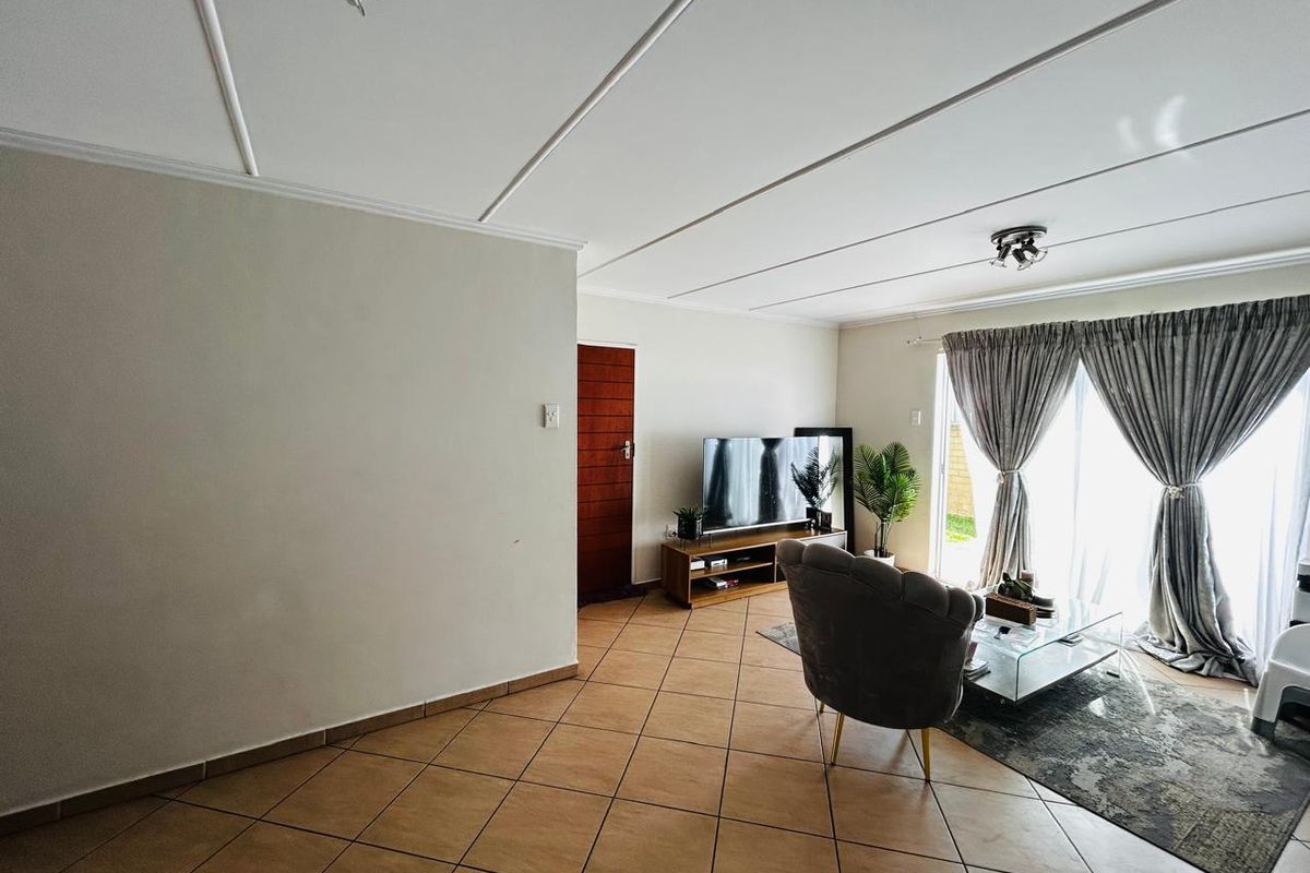 A living room featuring tiled flooring, a panelled ceiling with spotlights, and a sliding glass door providing access to the exterior.