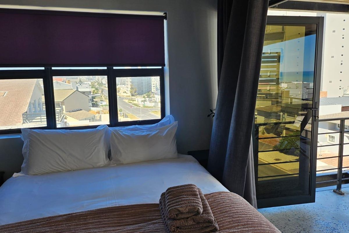 A bedroom featuring large windows and a glass door leading to a balcony, offering natural light and views of the surrounding area.