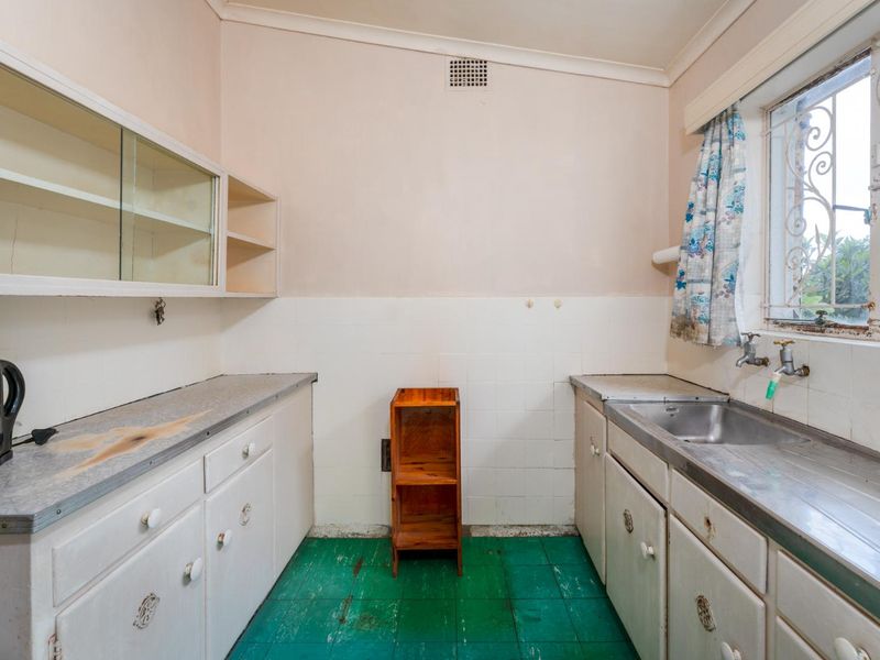 A dated kitchen featuring original cabinetry, a stainless steel sink, and tiled splashbacks, offering significant potential for a modern renovation.