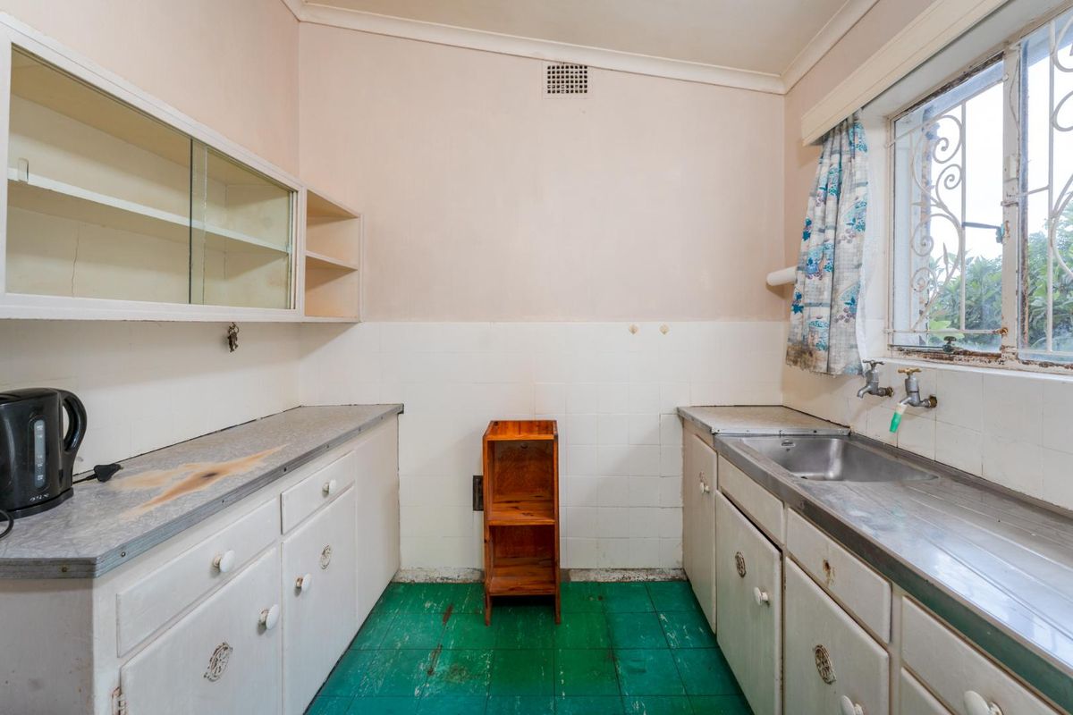 A dated kitchen featuring original cabinetry, a stainless steel sink, and tiled splashbacks, offering significant potential for a modern renovation.