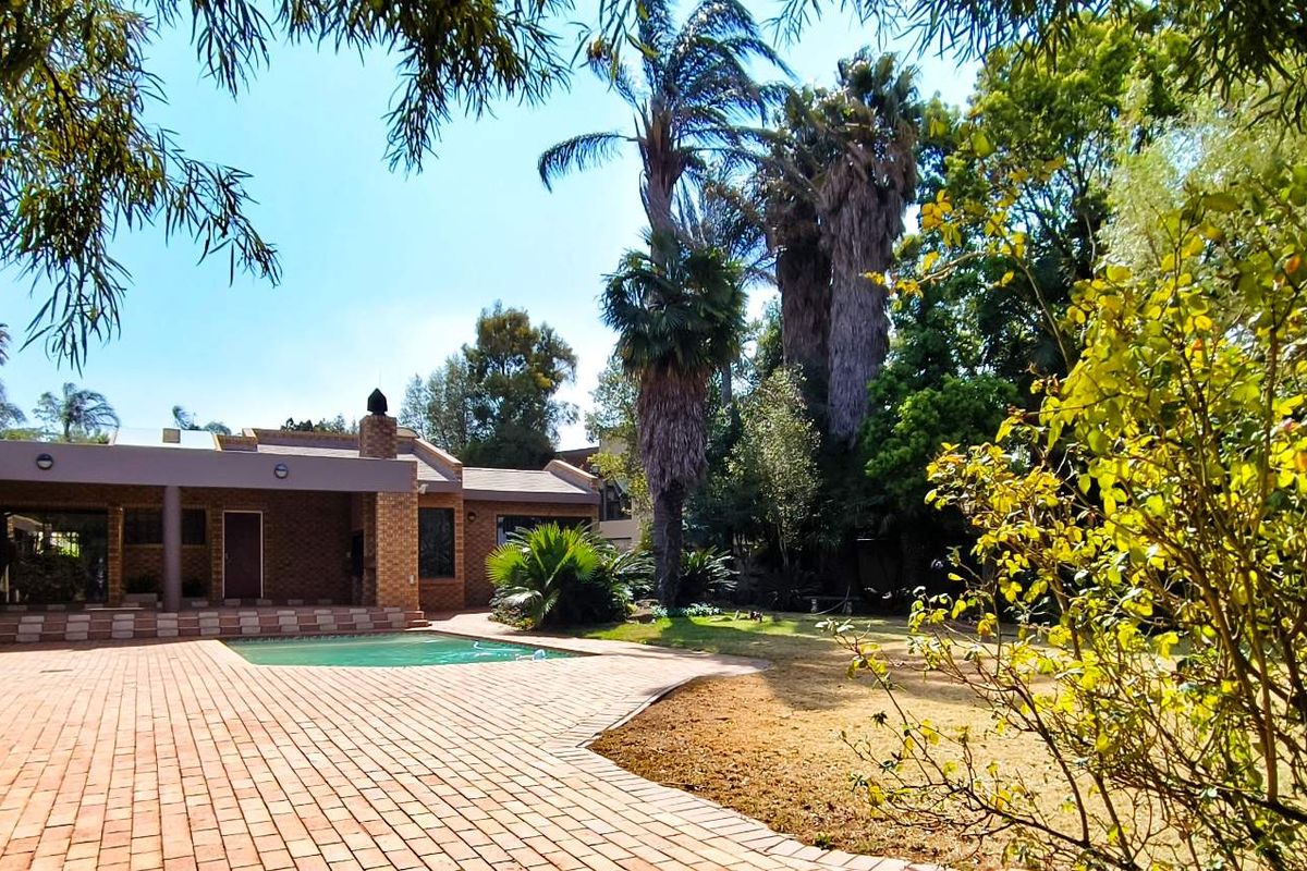 Spacious rear garden featuring a paved patio area, a swimming pool, and established trees, offering a private outdoor entertainment space.