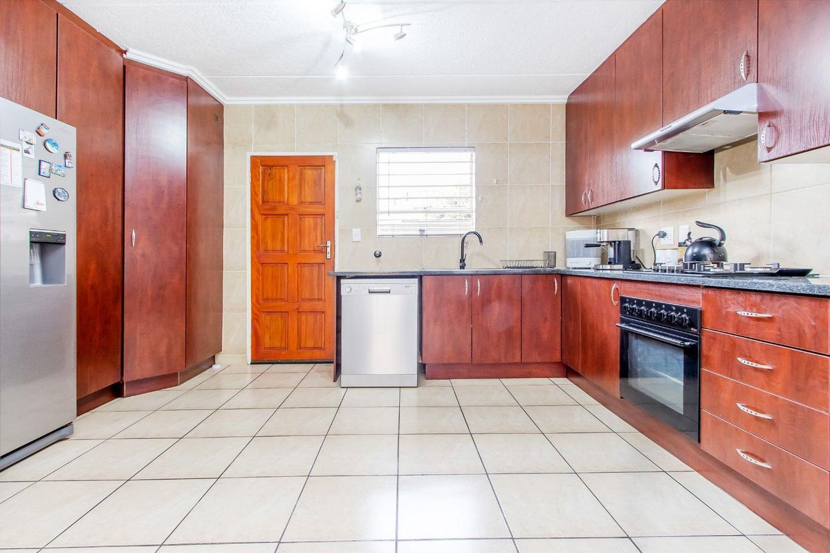 A functional kitchen featuring dark wood cabinetry, tiled flooring, a built-in oven, extractor fan, and a dedicated space for a dishwasher.