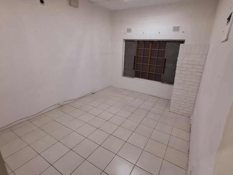 An empty office space featuring tiled flooring, an exposed brick pillar, and security bars on the window, requiring cosmetic updates and repairs.