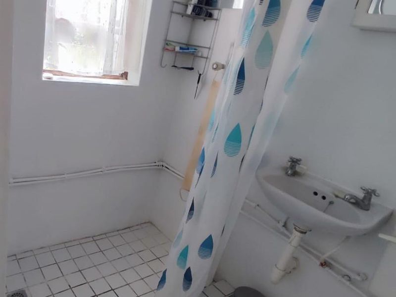 A compact bathroom featuring a pedestal basin, tiled flooring, and exposed plumbing, requiring modernization to improve functionality and aesthetic appeal.