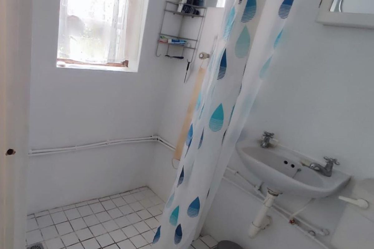 A compact bathroom featuring a pedestal basin, tiled flooring, and exposed plumbing, requiring modernization to improve functionality and aesthetic appeal.
