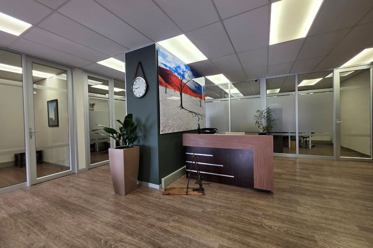 Professional office reception area featuring a modern reception desk, glass-partitioned office suites, suspended ceiling with recessed lighting, and wood-look laminate flooring.