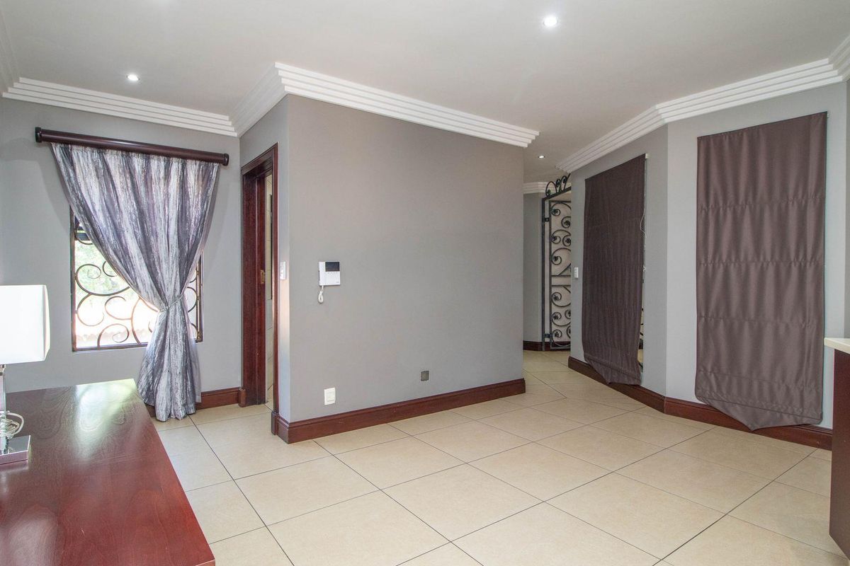 A spacious living area featuring neutral tiled flooring, decorative crown molding, and a security gate, providing a clean and functional layout.