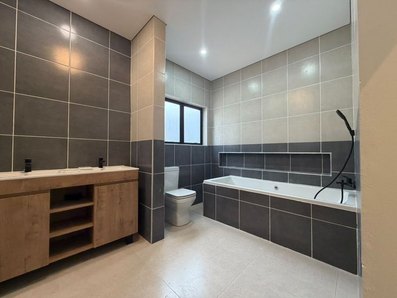 Modern bathroom featuring a double vanity, built-in bathtub with a recessed wall niche, and contemporary dark and light grey tiling.