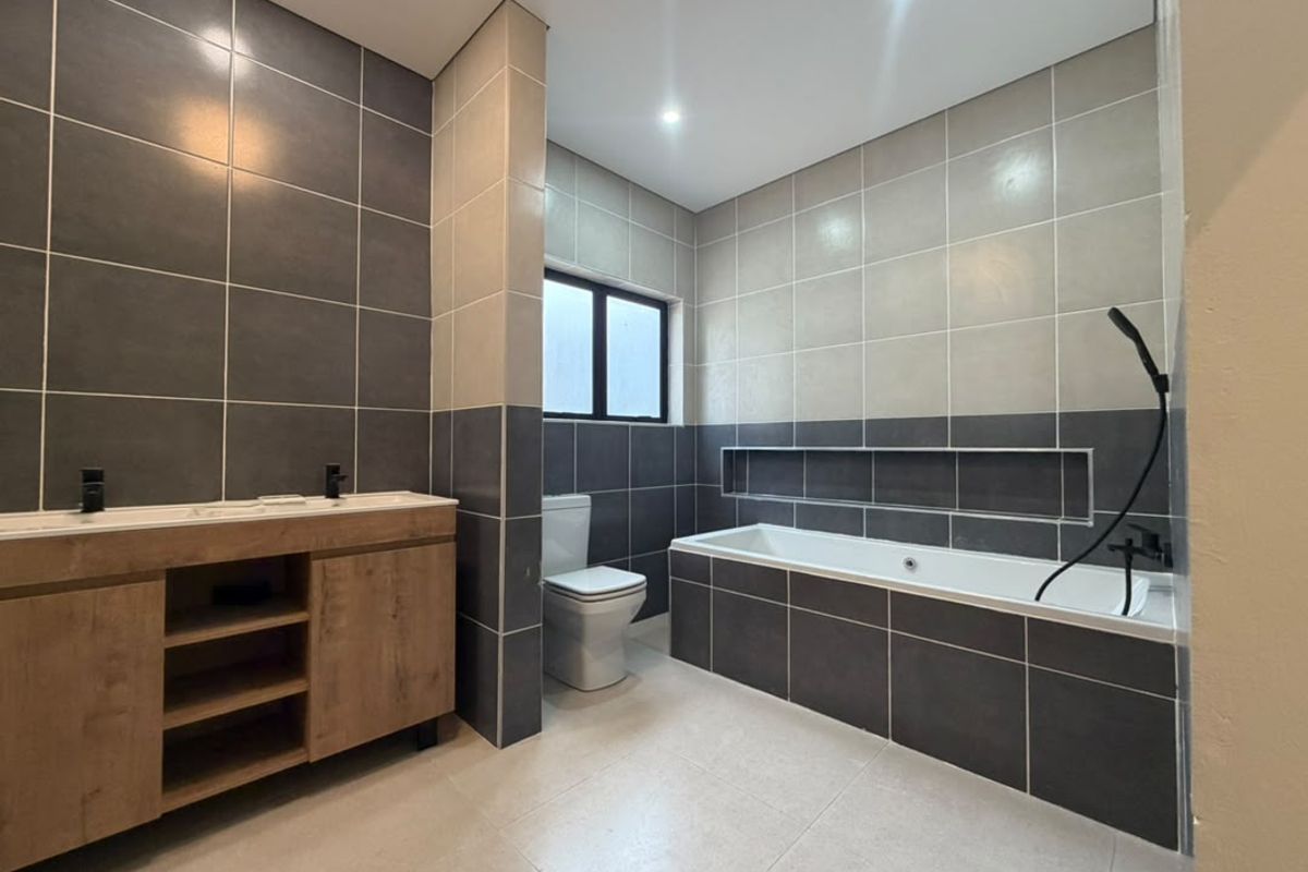 Modern bathroom featuring a double vanity, built-in bathtub with a recessed wall niche, and contemporary dark and light grey tiling.