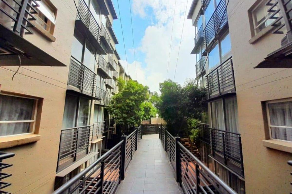 A view of the apartment complex walkway featuring modern architectural design, metal railings, and tiled flooring between building blocks.