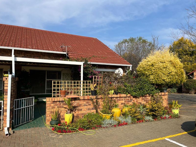 Front elevation of a retirement village unit featuring a brick facade, tiled roof, and a private paved patio area with established garden beds.