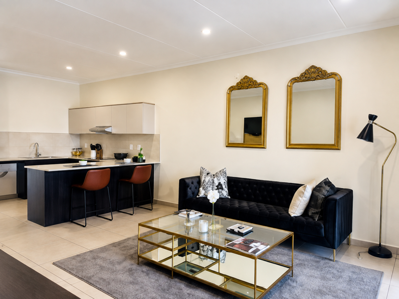 Modern open-plan living area featuring a sleek kitchen with stone countertops, integrated cabinetry, and tiled flooring, seamlessly flowing into the lounge space.