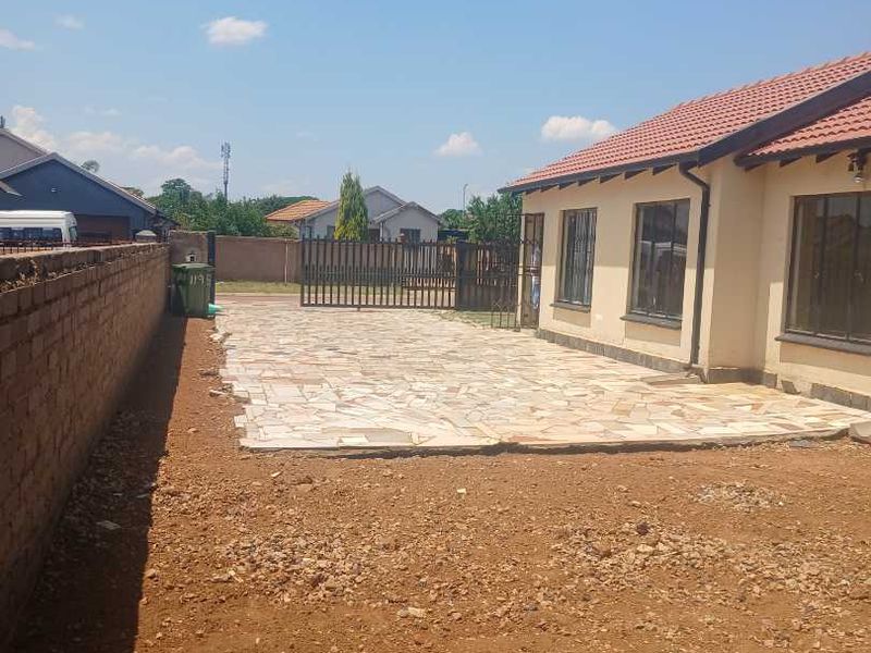 Rear exterior view featuring a paved patio area, boundary wall, and metal gate, with an unlandscaped garden space requiring further development.