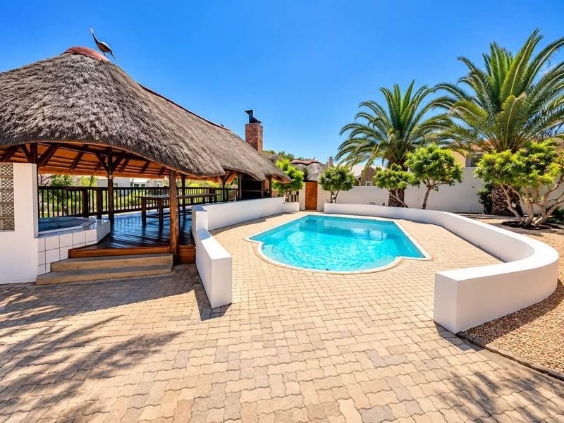 Outdoor entertainment area featuring a swimming pool, paved surround, and a thatched lapa with a built-in fireplace and timber decking.