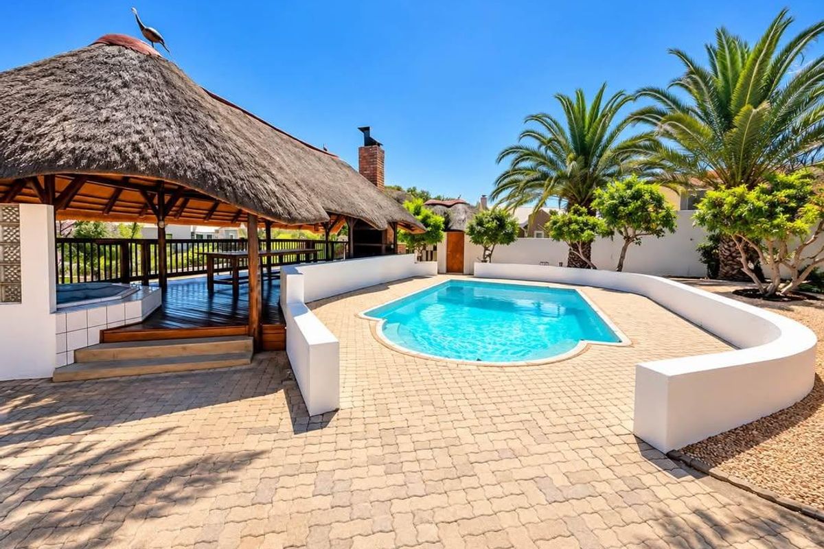 Outdoor entertainment area featuring a swimming pool, paved surround, and a thatched lapa with a built-in fireplace and timber decking.