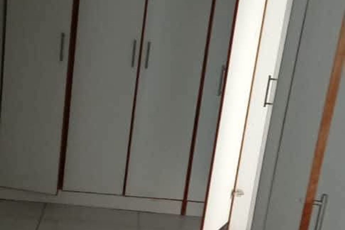 A bedroom featuring white built-in cupboards with wooden trim and light-colored tiled flooring.