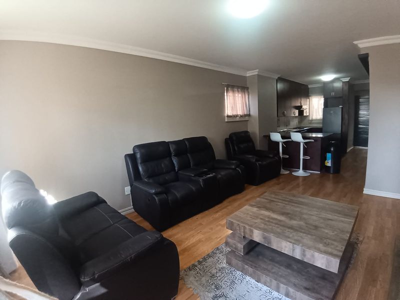 Open plan living area featuring laminate flooring and a functional kitchen with built-in cabinetry and a breakfast counter.