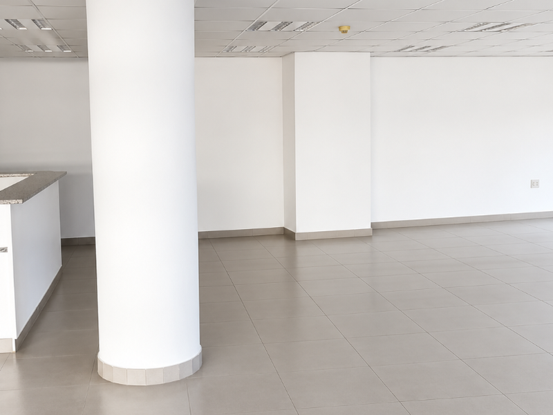 A bright, open-plan office space featuring neutral ceramic floor tiles, a suspended ceiling with recessed lighting, and a prominent structural column.