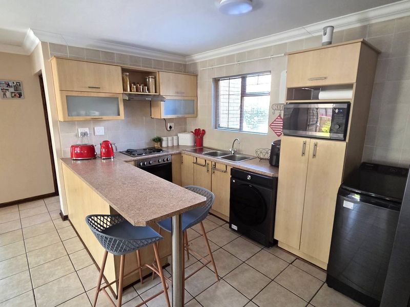 Functional kitchen featuring light wood cabinetry, laminate countertops, a breakfast nook, and tiled finishes, offering a practical layout for daily meal preparation.