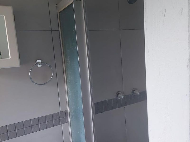 A functional bathroom featuring a shower enclosure with sliding doors, a wall-mounted medicine cabinet, and grey tiled walls with a decorative mosaic border.
