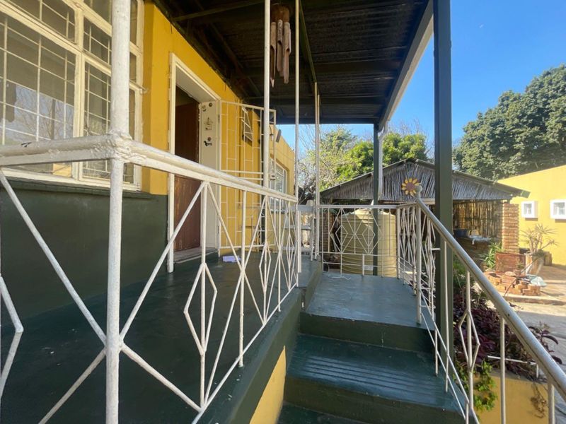A covered outdoor patio area featuring metal railings and concrete steps, providing access to the home's exterior and garden space.