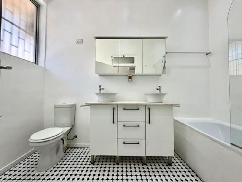 A clean, modern bathroom featuring a double vanity with vessel sinks, a medicine cabinet, a toilet, and a bathtub with a glass screen.