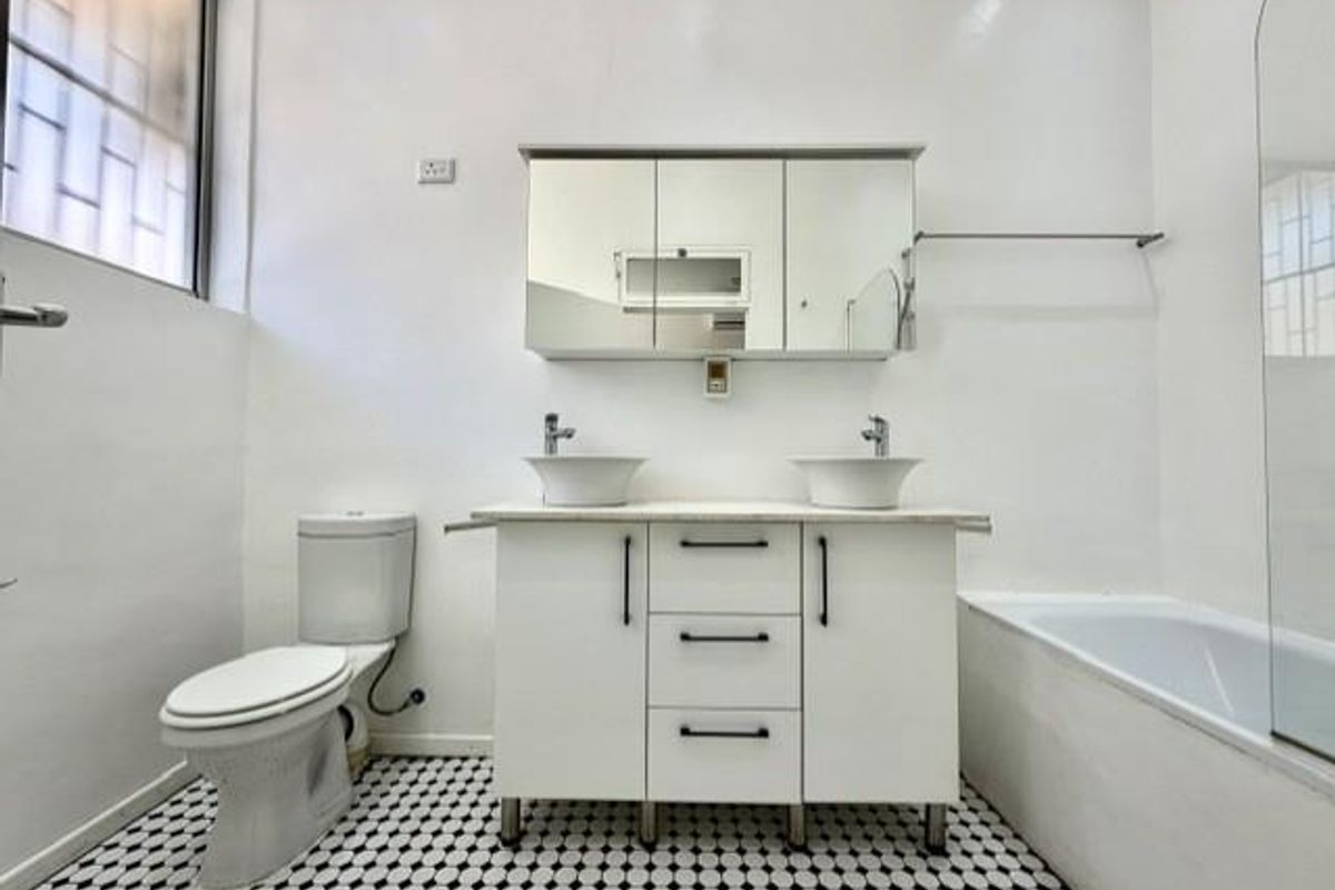 A clean, modern bathroom featuring a double vanity with vessel sinks, a medicine cabinet, a toilet, and a bathtub with a glass screen.