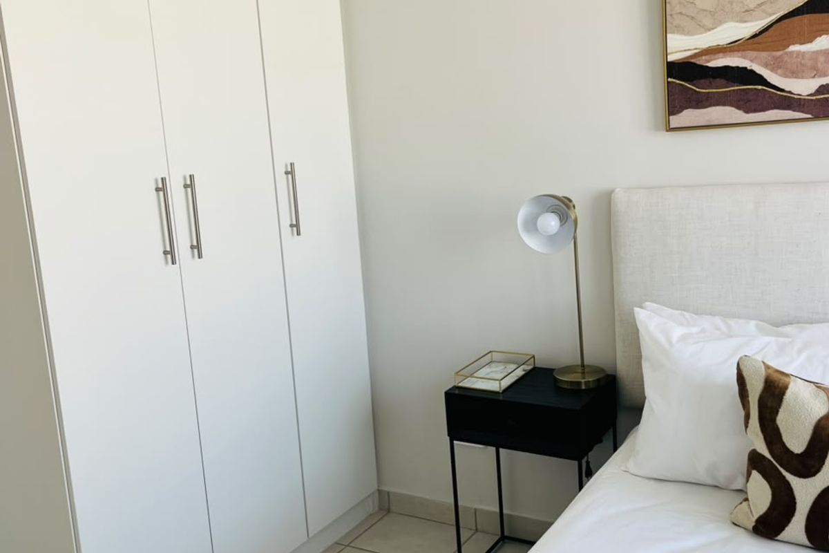 A well-maintained bedroom featuring a modern white built-in wardrobe and neutral tiled flooring.