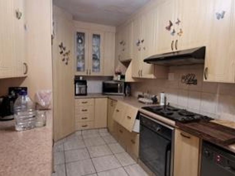 A functional kitchen featuring light wood-finish cabinetry, tiled flooring, a built-in oven with gas hob, and an extractor fan.