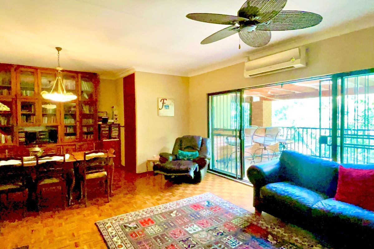 Spacious living area featuring parquet flooring, built-in wooden cabinetry, ceiling fan, wall-mounted air conditioning unit, and sliding glass doors leading to an outdoor patio.