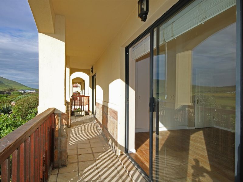 A spacious covered balcony featuring tiled flooring, stone accents, and a wooden balustrade, offering direct access to the interior through sliding glass doors.