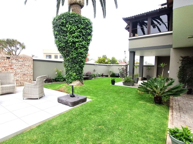 A well-maintained rear garden featuring a tiled patio area, lush lawn, and a covered balcony overlooking the outdoor space.