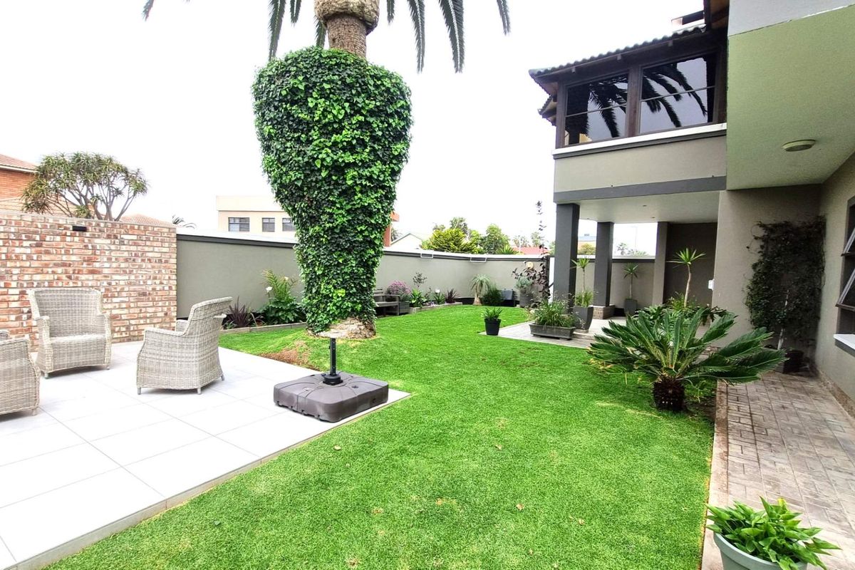 A well-maintained rear garden featuring a tiled patio area, lush lawn, and a covered balcony overlooking the outdoor space.