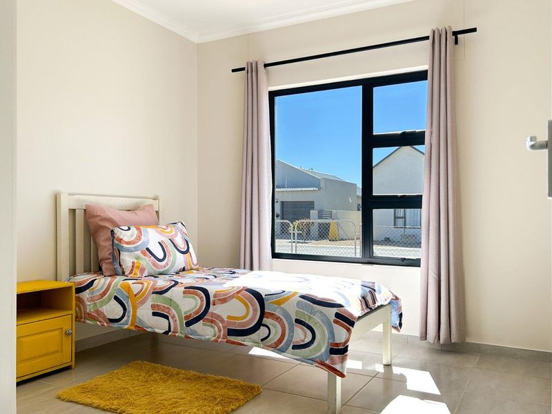 A bright and well-maintained bedroom featuring neutral walls, tiled flooring, and a large aluminium-framed window allowing for ample natural light.