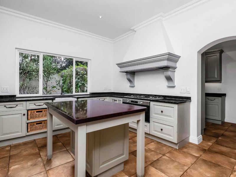 A well-appointed kitchen featuring grey cabinetry, granite countertops, a central island, built-in oven, gas hob, and classic ceramic tile flooring.