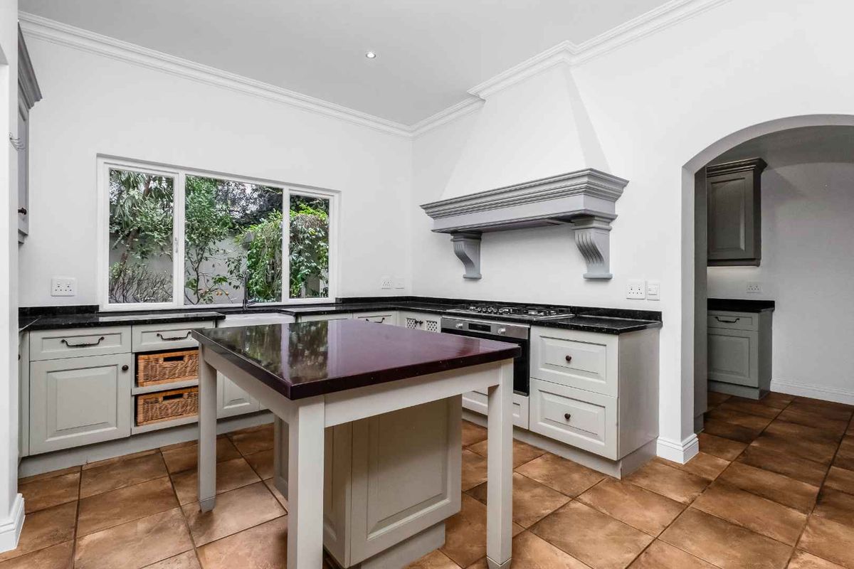 A well-appointed kitchen featuring grey cabinetry, granite countertops, a central island, built-in oven, gas hob, and classic ceramic tile flooring.