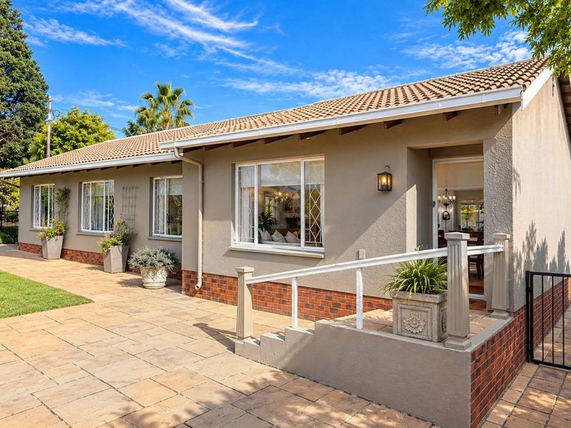 A well-maintained rear exterior view featuring a paved patio area, brick and plaster facade, and a tiled roof with guttering.
