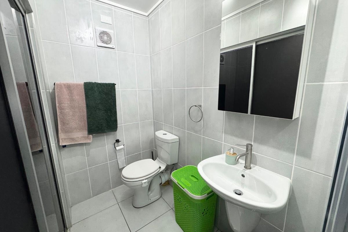 A clean and functional bathroom featuring full-height ceramic wall tiling, a pedestal washbasin with chrome mixer tap, a toilet, and a glass shower enclosure.