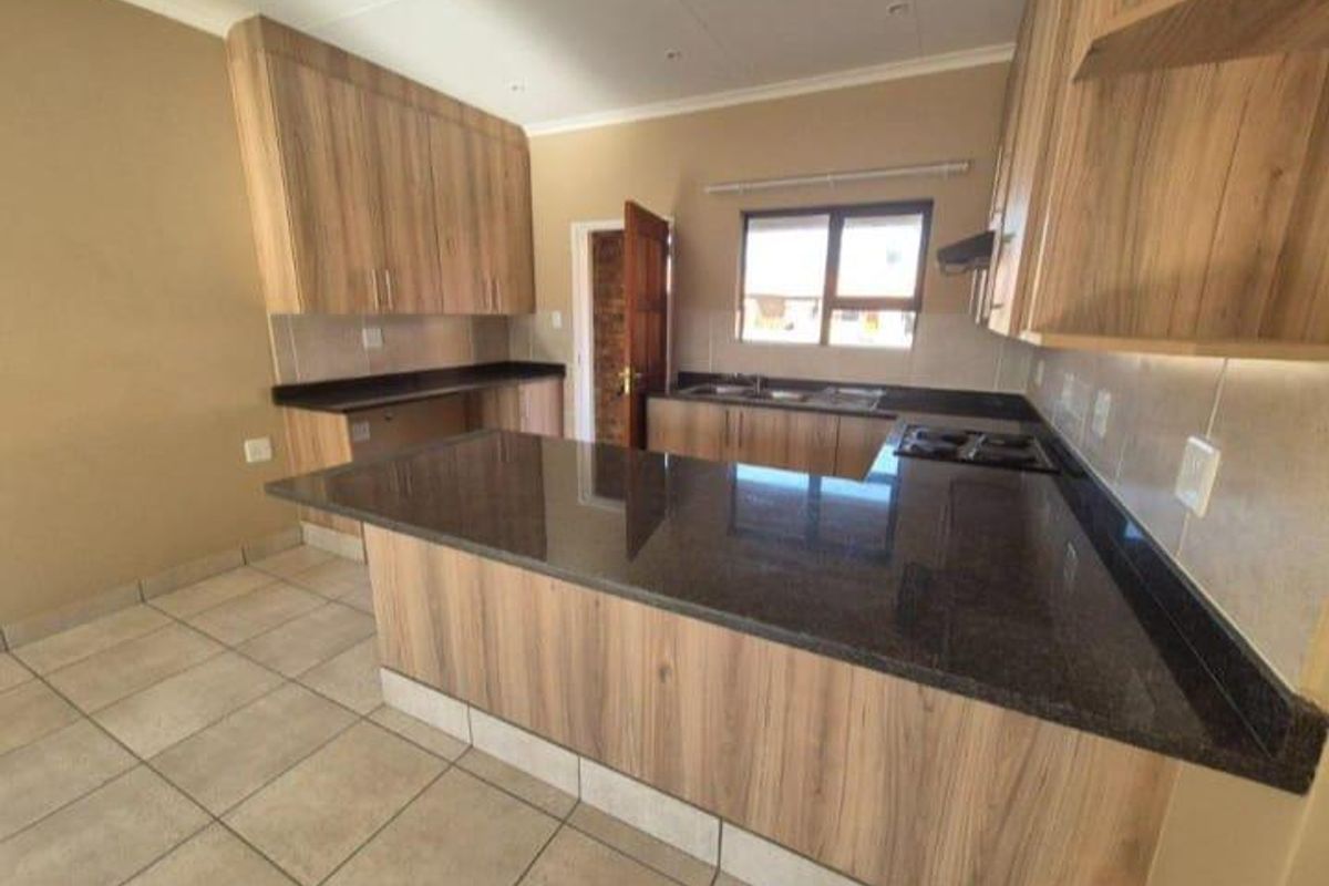 A modern, empty kitchen featuring wood-look laminate cabinetry, dark granite countertops, a built-in hob, and tiled flooring, offering a clean and functional workspace.