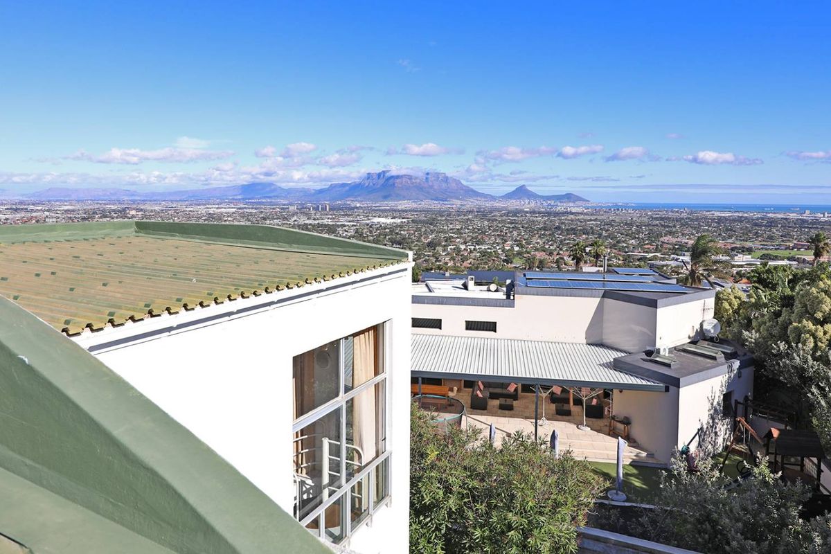 Elevated aerial view showcasing the property's roof structure, rear patio area, and expansive panoramic views of the surrounding landscape and distant mountains.
