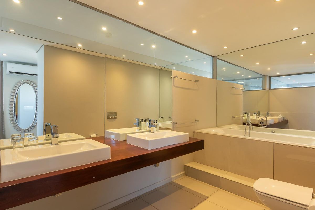 Modern bathroom featuring a floating timber vanity with dual vessel sinks, a built-in bathtub, large wall-to-wall mirrors, and recessed ceiling lighting.
