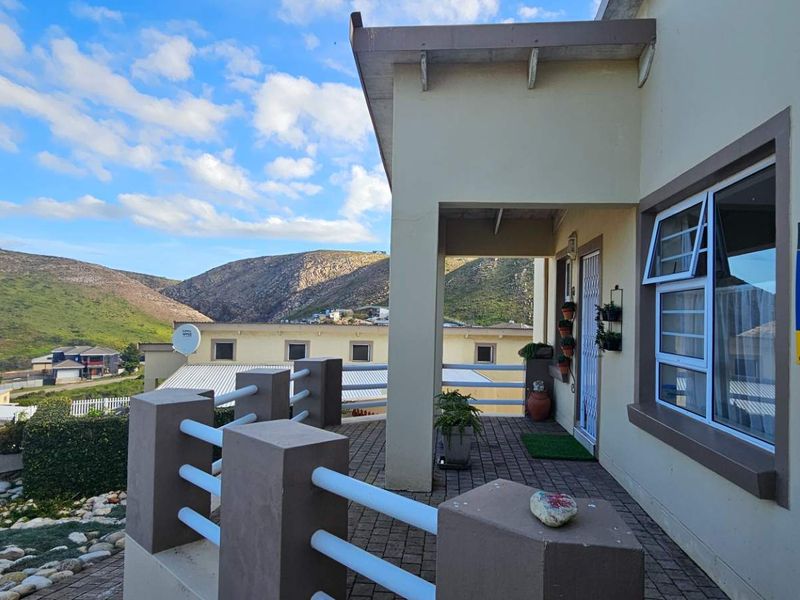 A covered patio area featuring paved flooring and railings, offering scenic views of the surrounding landscape and neighboring properties.