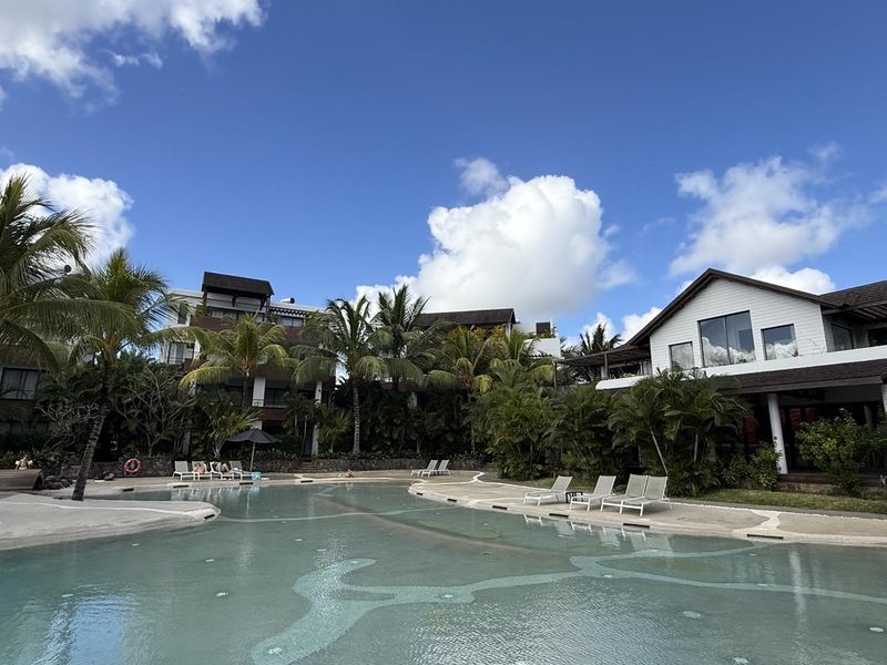 A well-maintained outdoor swimming pool area surrounded by lush tropical landscaping and modern residential building architecture.