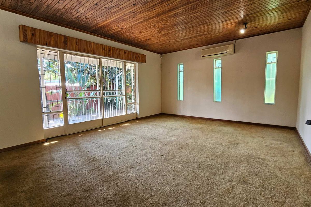 Spacious living area featuring a timber-clad ceiling, wall-mounted air conditioning unit, and large sliding glass doors with security gates leading to the garden.
