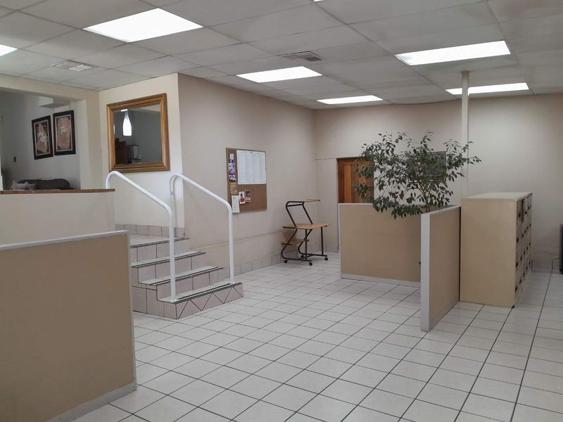 Open-plan office space featuring ceramic tiled flooring, suspended ceiling with recessed lighting, and built-in partitions with a central staircase.